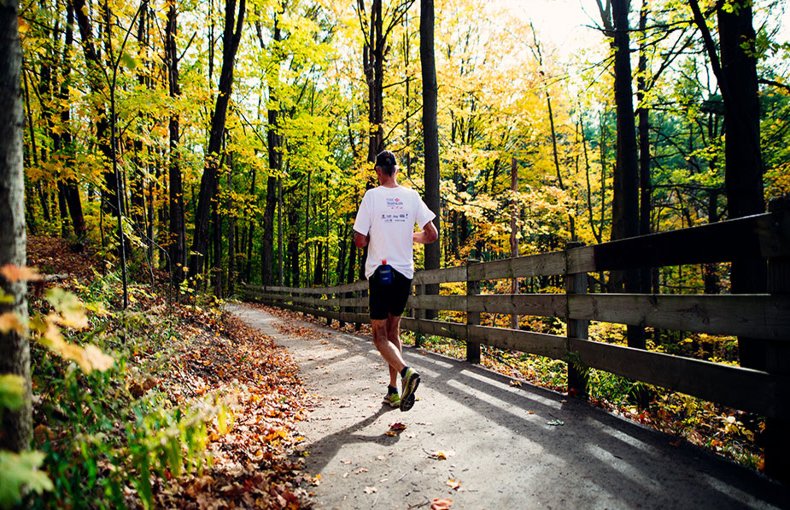Person running along a trail in the woods during the fall - fallen leaves along the edge of the path and colourful leaves on the trees.