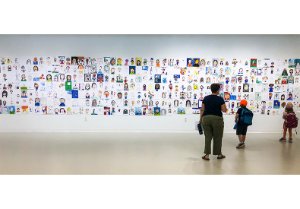 An adult and two children looking at a gallery wall of portraits An adult and two children looking at a gallery wall of portraits