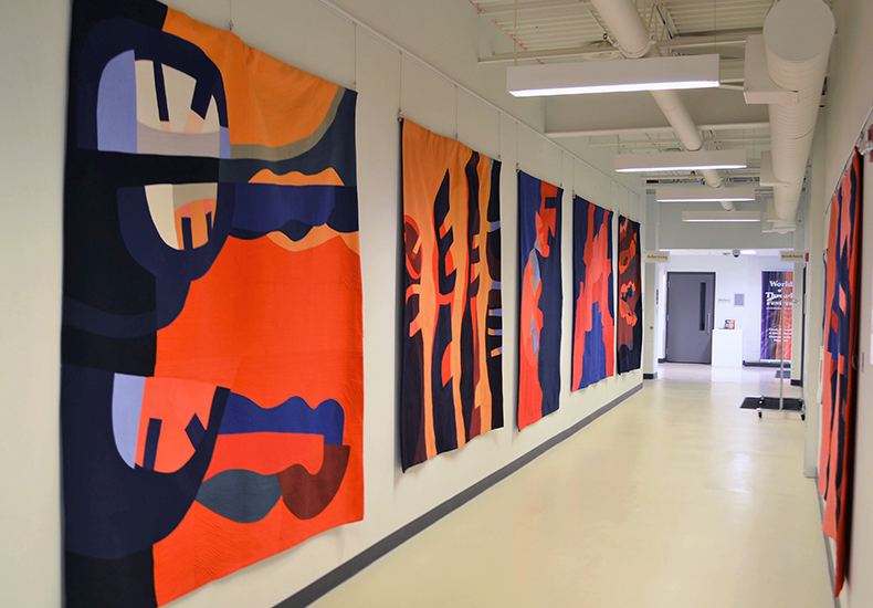 Orange and black quilts displayed on corridor walls for the World of Threads Festival