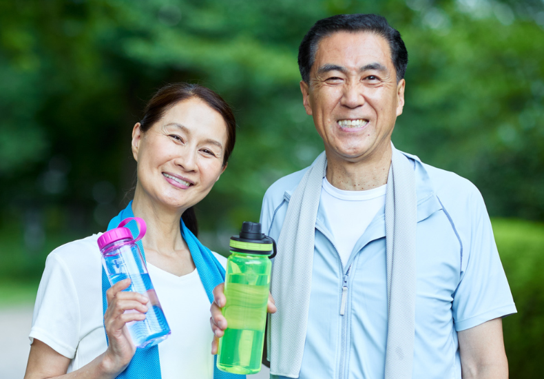 Two older adults each holding a reusable water bottle with a towel around their shoulders