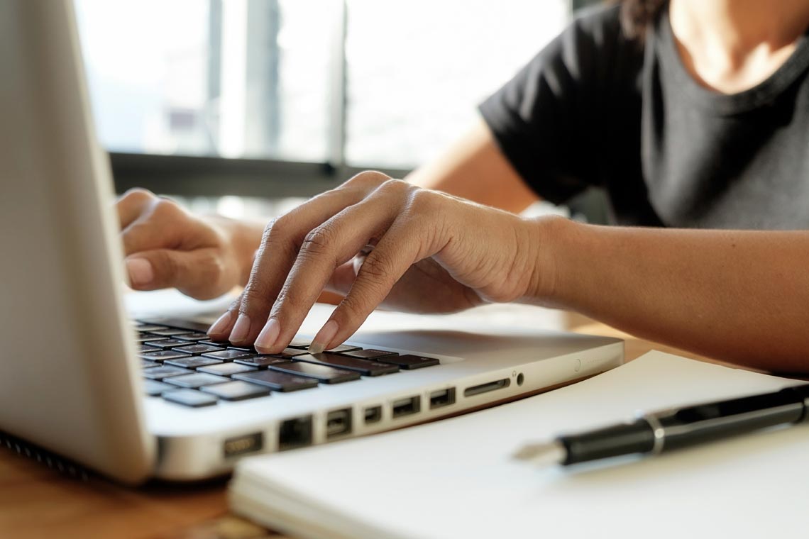 Close up of a person's hands typing on a laptop keyboard.