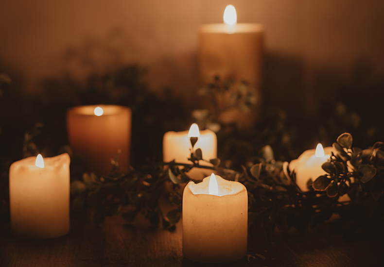 Lit candles and greenery on a table in the dark.