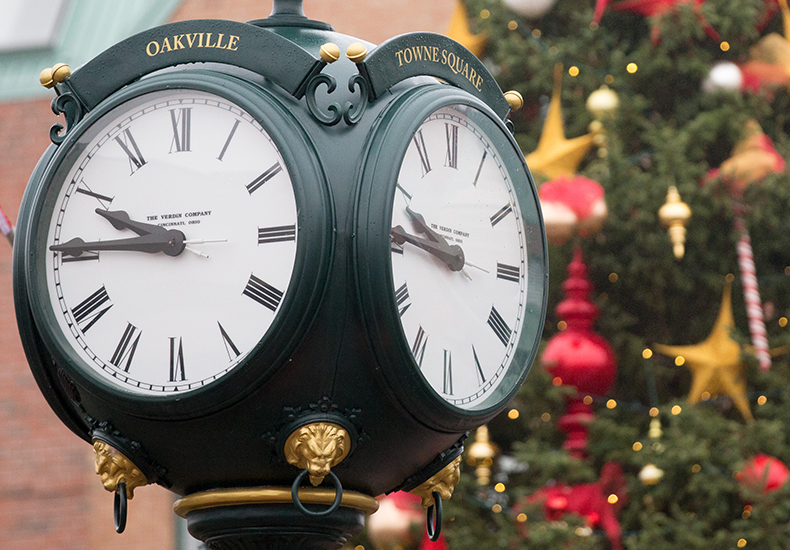The Towne Square Clock in Downtown Oakville with a pine tree decorated for the holidays in the background.