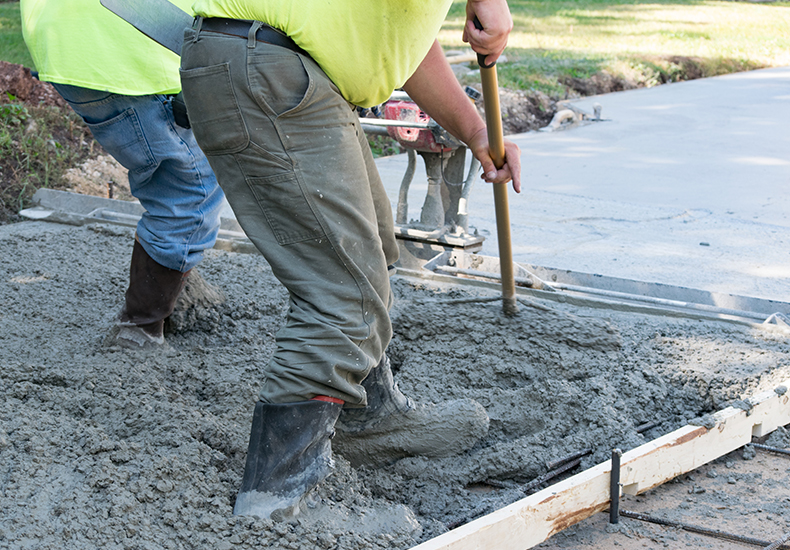 Workers pouring and finishing a concrete slab driveway.
